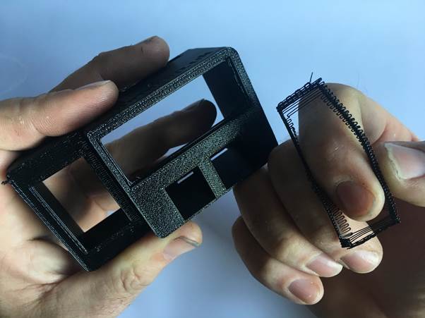 Close-up of a person holding a 3D printed black clock housing while removing a support material piece from it.