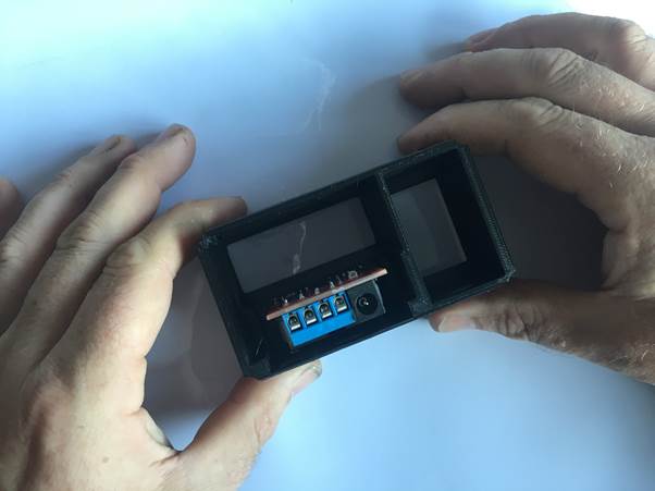 Hands holding a 3D-printed clock housing with an electronic module visible inside.