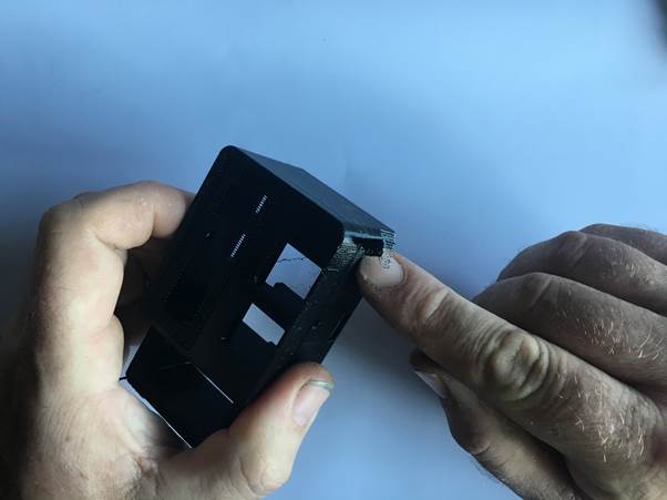 A person holding a 3D-printed clock housing and carefully removing support material from the edge.