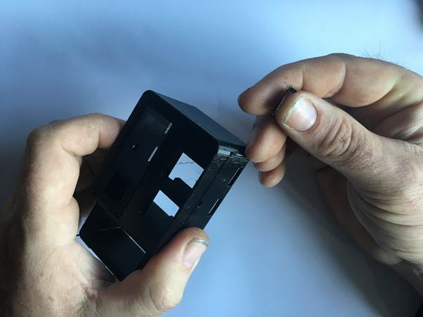 A person holding a black 3D printed clock casing, with a small part in their other hand, preparing to clean up support material.