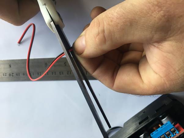 A person using wire cutters to cut a red wire while holding a ruler next to it.