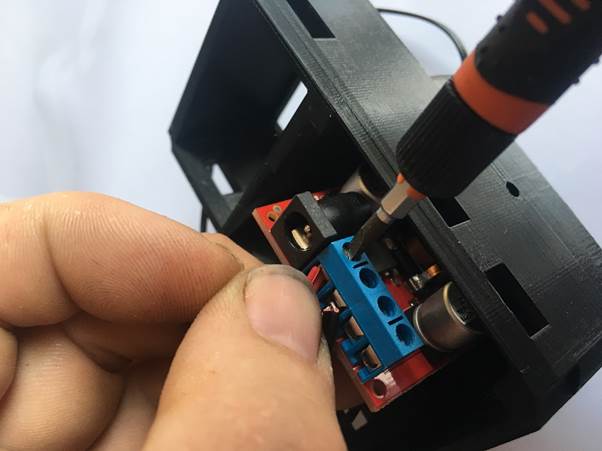 A close-up image of a hand holding a piece of electronic equipment, connecting wires to a blue terminal block using a screwdriver.