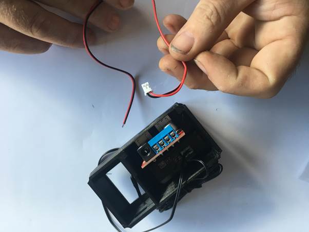 Hands connecting red and black wires to a USB module inside a clock assembly.