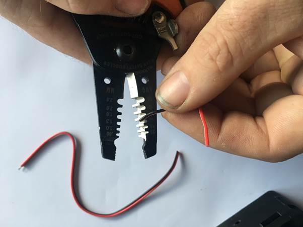 A person using wire strippers to prepare a black wire for connection, with a red wire visible nearby.