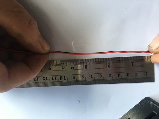 A person's hand holding a red wire against a metal ruler, measuring approximately 4 inches in length.