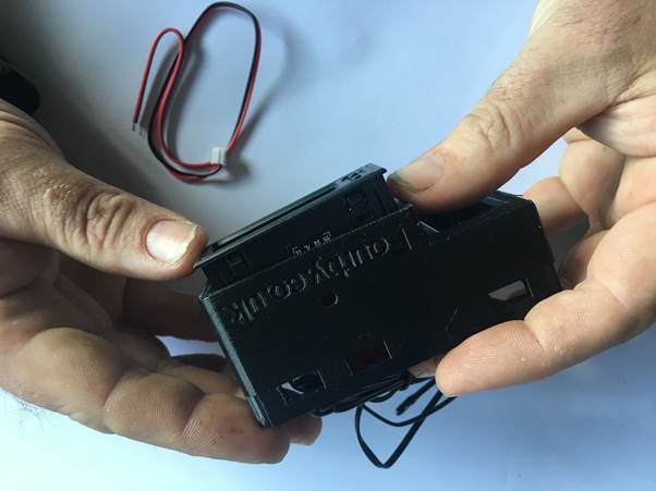 A person holding a black USB clock module, with wiring visible in the background.