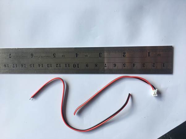 A red and black wire with a connector on one end, positioned on a ruler for measurement.