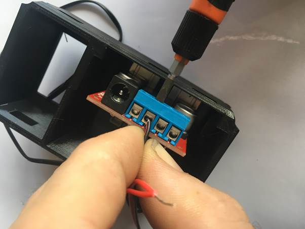 A close-up of a hand connecting wires to a terminal block in a 3D printed clock module using a screwdriver.