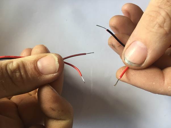 Two wires being prepared for connection, one red and one black, with stripped ends visible.
