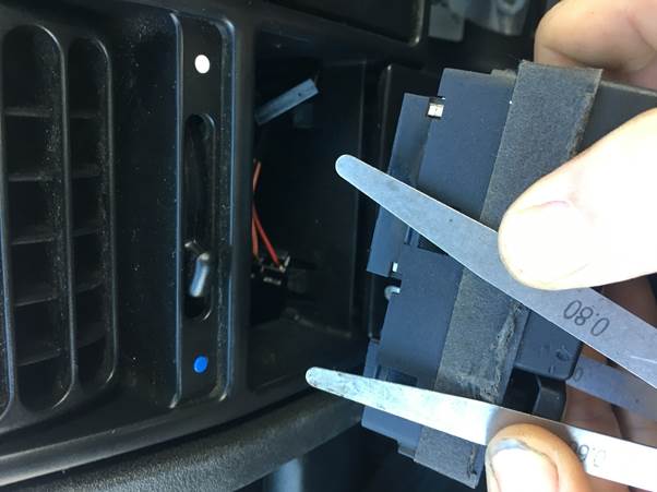 Close-up of hands using feeler gauges to remove the old clock from a car dashboard.