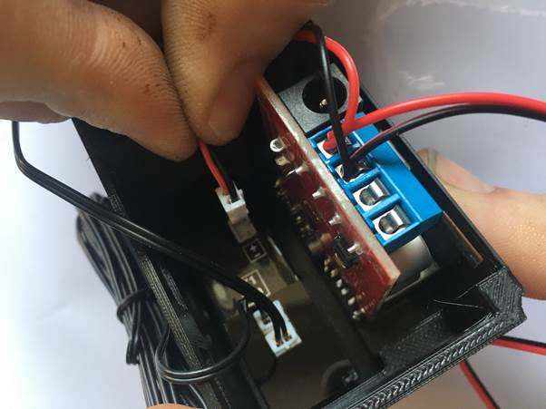 A person connecting wires to the terminal block inside a Fourby USB clock module, with red and black wires visible.