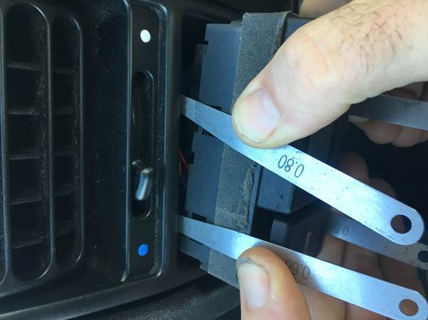 Hands using shims to remove a clock from a vehicle dashboard.