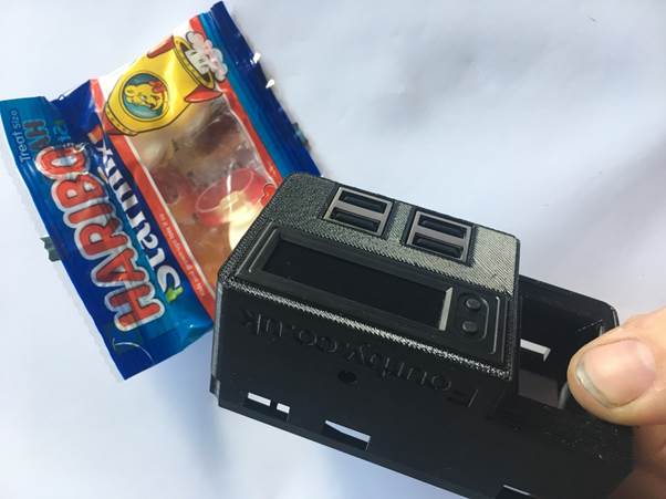 A hand holding a 3D printed USB module for a clock kit next to a packet of Haribo gummy candies.