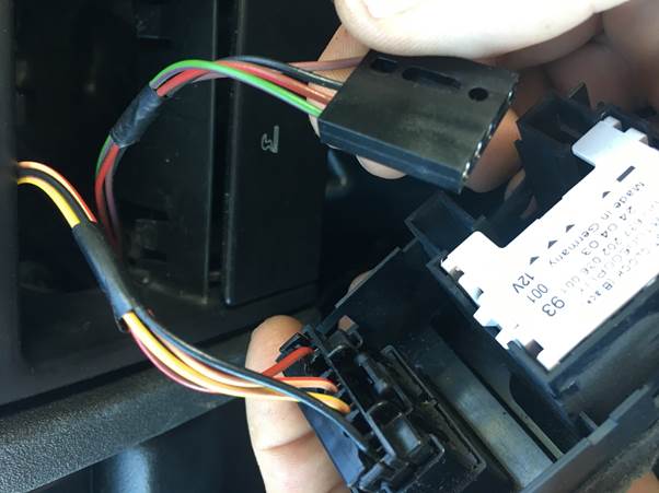 Close-up of a hand holding an electrical plug with colored wires, being connected to a dash-mounted clock module.