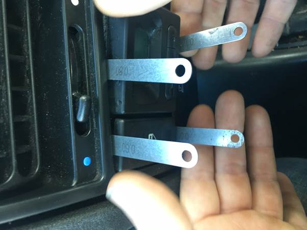 Hand holding shims inserted into a car dashboard clock removal mechanism.