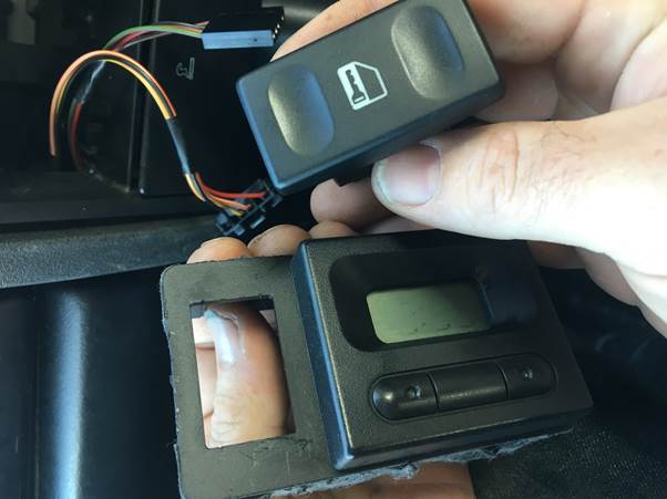 A person holding a car clock assembly and switch while preparing for installation, with visible wiring and a dashboard background.