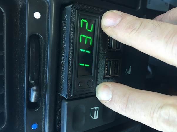 A close-up view of a Fourby multifunction USB clock installed in a car dashboard, displaying the time '2:11' with a finger poised to touch the buttons.
