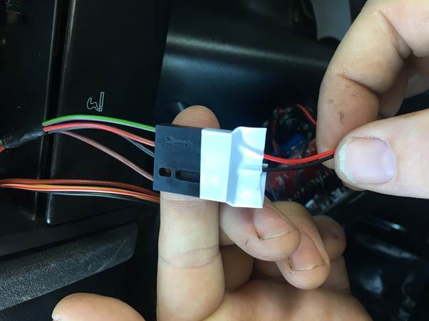 A close-up image of a hand holding a multi-plug connector with wires for a Fourby USB Clock installation, featuring labeled connections for easier setup.