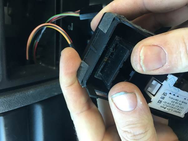 Close-up of a hand holding a car switch module while connecting wires inside a vehicle's dashboard.