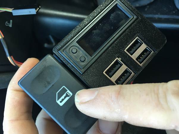 A hand holding a USB module with a display and buttons, positioned next to a car's interior.