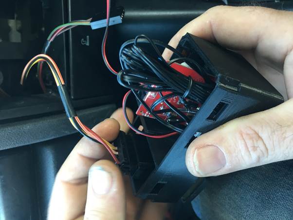 A person holding a small black electronic device with multiple connected wires inside, preparing it for installation in a vehicle.